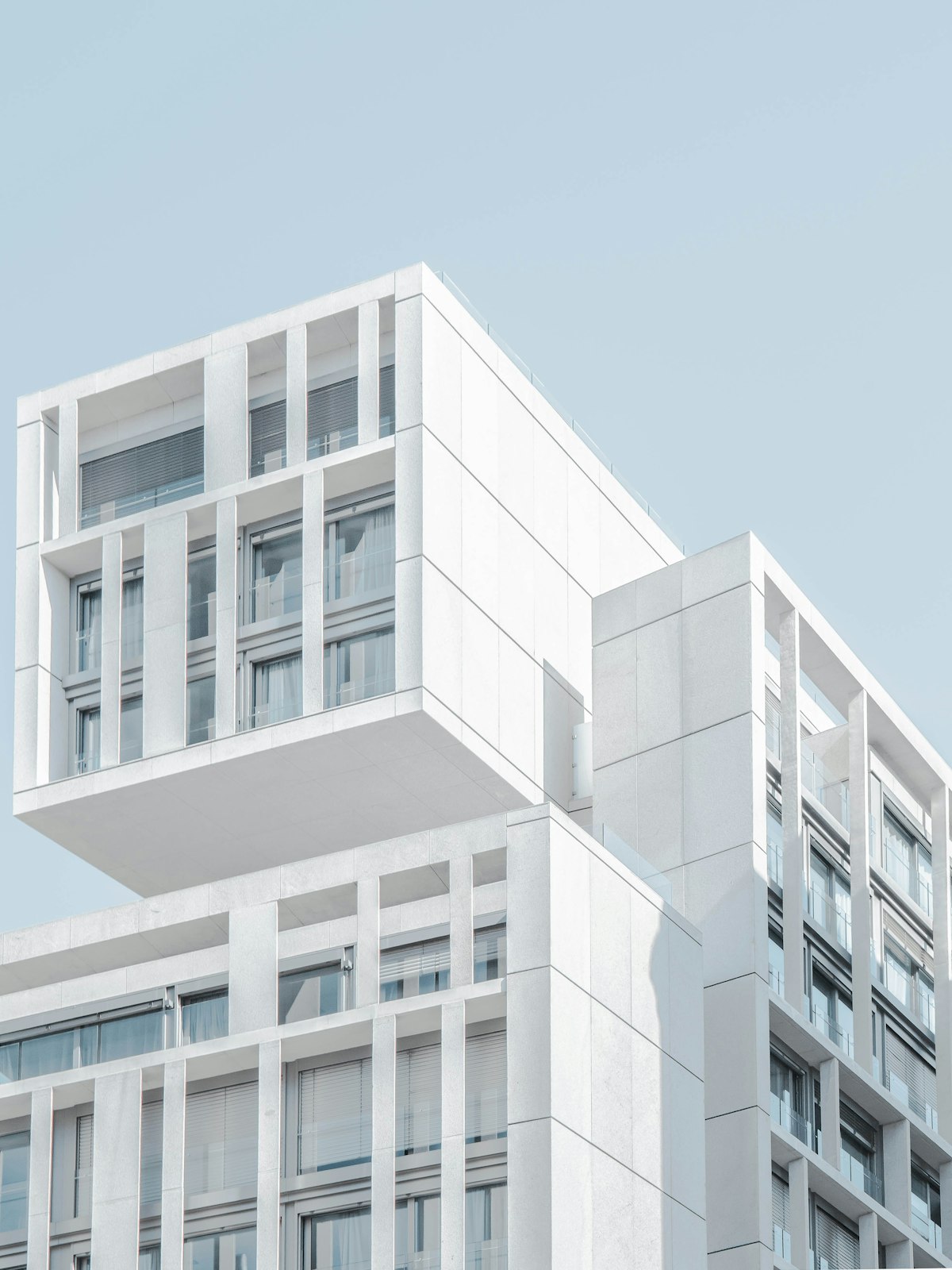 Stacked white residential blocks with deep-set windows against a pale blue sky